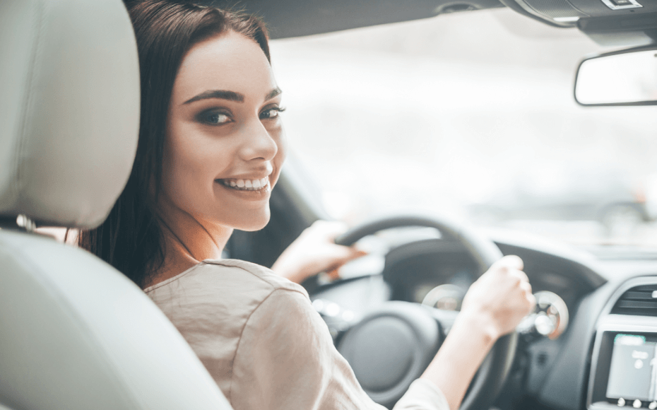 a beautiful girl with dark hair is looking over her shoulder as she grips the steering wheel