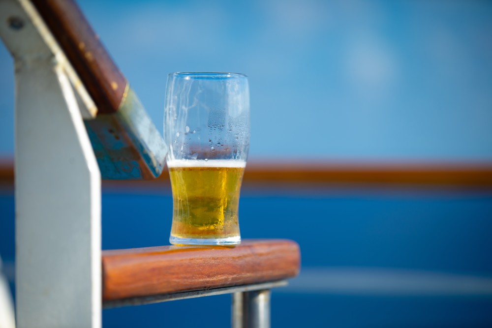 Half,Drunk,Beer,On,Bench,With,Blue,Sea,And,Sky