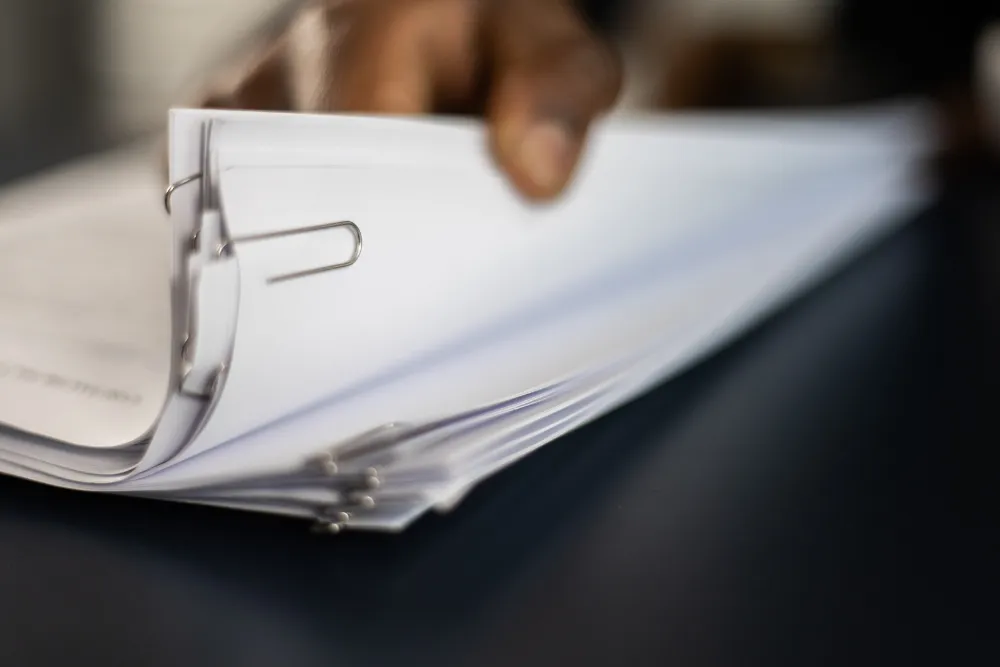 Hand holding a ring binder with papers fanned out on a dark desk surface